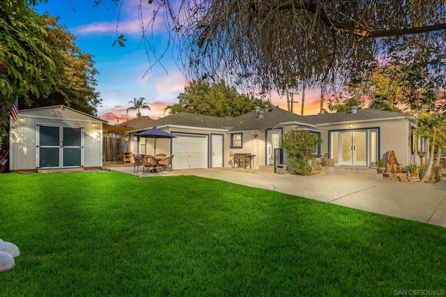 back house at dusk featuring a patio area, a lawn, french doors, and a storage unit