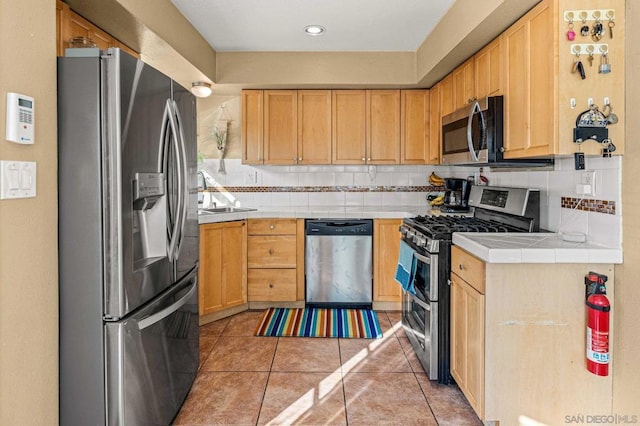 kitchen featuring light tile patterned floors, appliances with stainless steel finishes, decorative backsplash, tile countertops, and light brown cabinets