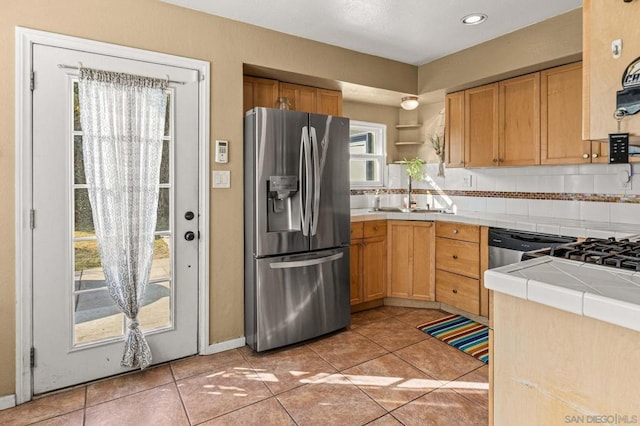 kitchen featuring sink, light tile patterned floors, stainless steel fridge, decorative backsplash, and tile countertops