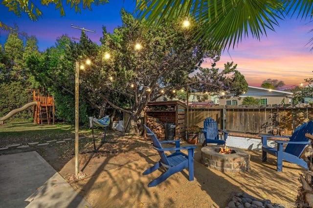 yard at dusk featuring a playground, a patio area, and an outdoor fire pit