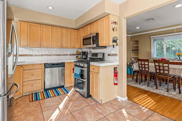 kitchen with tasteful backsplash, appliances with stainless steel finishes, light brown cabinetry, and light tile patterned floors