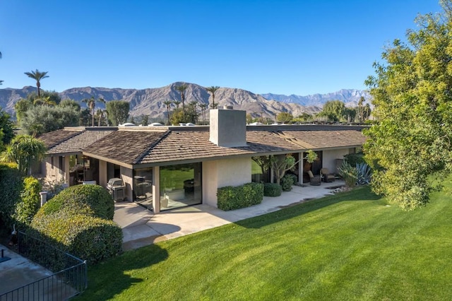 back of property featuring a mountain view, a patio area, and a lawn