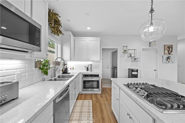 kitchen featuring sink, white cabinetry, hanging light fixtures, stainless steel appliances, and light stone countertops