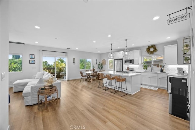 kitchen featuring pendant lighting, stainless steel appliances, a center island, light hardwood / wood-style floors, and white cabinets