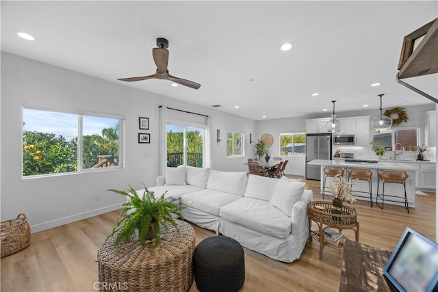 living room with ceiling fan, plenty of natural light, sink, and light wood-type flooring