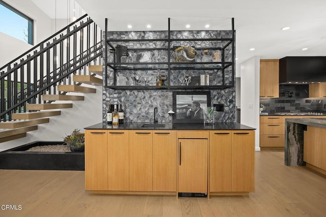 bar featuring wall chimney exhaust hood, sink, light hardwood / wood-style flooring, and backsplash