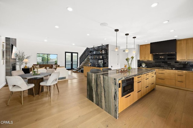 kitchen with built in microwave, pendant lighting, light wood-type flooring, and dark stone counters