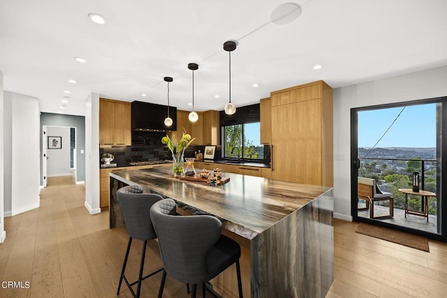 kitchen featuring a spacious island, light hardwood / wood-style flooring, a kitchen breakfast bar, pendant lighting, and decorative backsplash