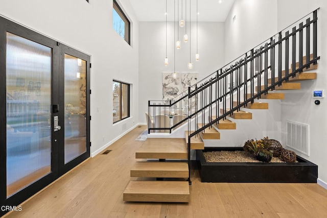 stairs with wood-type flooring, a towering ceiling, and french doors