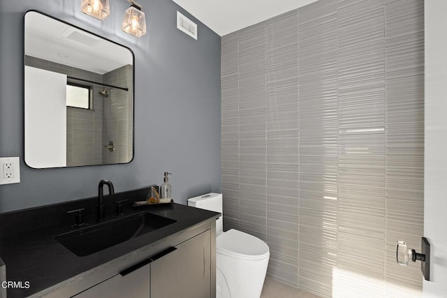 bathroom with a tile shower, vanity, tile walls, and toilet