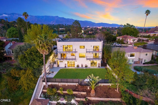 back house at dusk featuring a balcony, a yard, and a mountain view