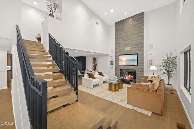 living room featuring a high ceiling, a tiled fireplace, and wood-type flooring