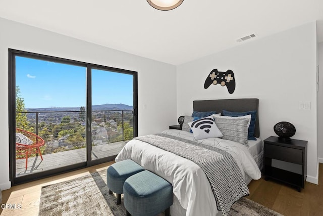 bedroom featuring multiple windows, wood-type flooring, a mountain view, and access to outside