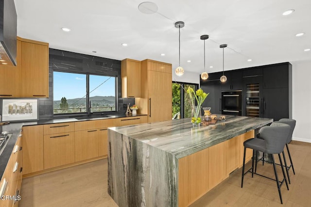 kitchen featuring decorative light fixtures, sink, a breakfast bar area, light wood-type flooring, and a spacious island