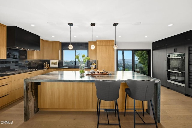 kitchen with light hardwood / wood-style flooring, black double oven, tasteful backsplash, a kitchen island, and decorative light fixtures