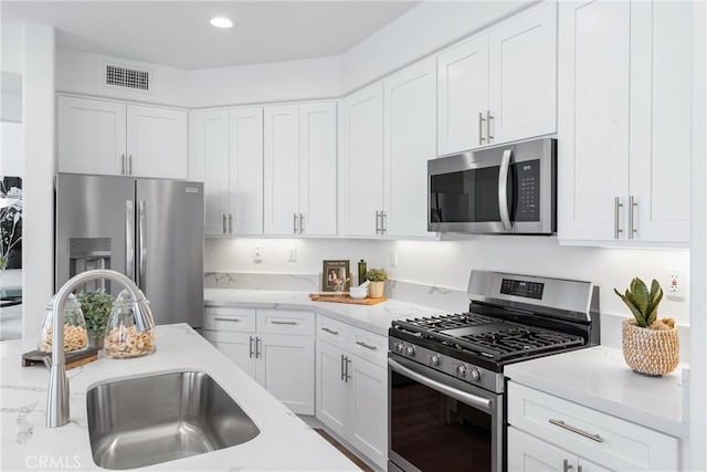 kitchen with appliances with stainless steel finishes, sink, white cabinets, and light stone counters