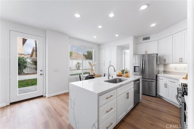 kitchen featuring stainless steel appliances, white cabinetry, sink, and a kitchen island with sink