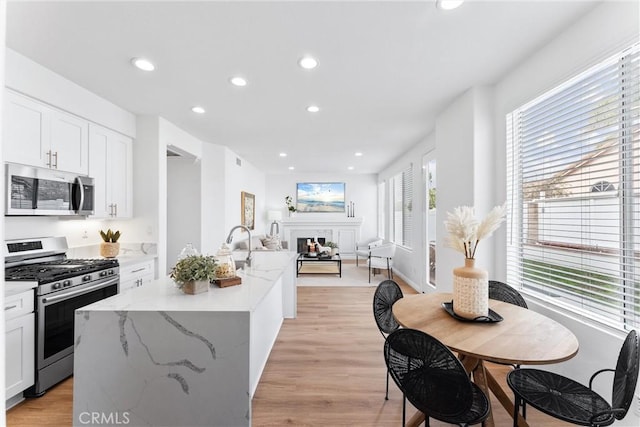 kitchen with white cabinetry, light wood-type flooring, an island with sink, stainless steel appliances, and light stone countertops