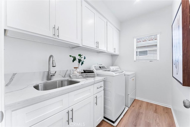 laundry area with light hardwood / wood-style floors, sink, washing machine and dryer, and cabinets