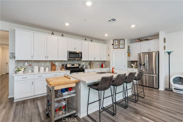 kitchen featuring a breakfast bar, white cabinetry, appliances with stainless steel finishes, hardwood / wood-style flooring, and a kitchen island with sink