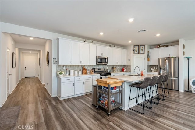 kitchen with a kitchen bar, sink, white cabinetry, an island with sink, and stainless steel appliances