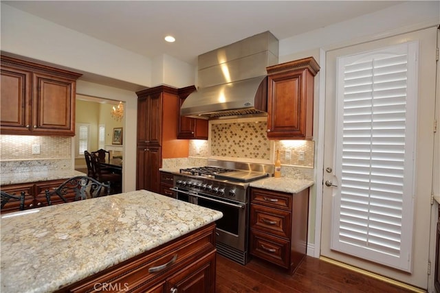 kitchen with tasteful backsplash, dark hardwood / wood-style flooring, double oven range, light stone counters, and wall chimney exhaust hood