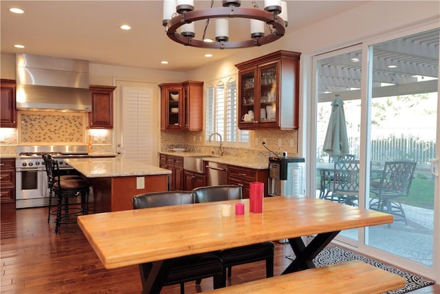 kitchen with sink, appliances with stainless steel finishes, an inviting chandelier, a kitchen island, and wall chimney exhaust hood