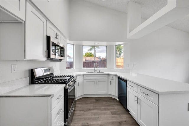 kitchen with sink, appliances with stainless steel finishes, kitchen peninsula, hardwood / wood-style floors, and white cabinets