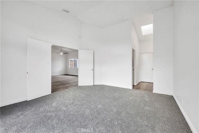 carpeted spare room with a skylight and high vaulted ceiling