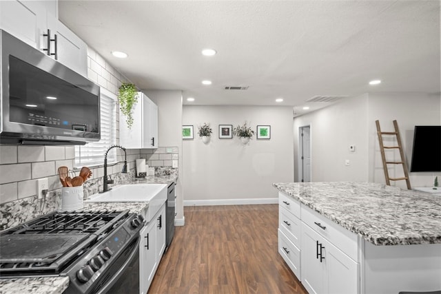 kitchen with appliances with stainless steel finishes, sink, white cabinets, dark hardwood / wood-style flooring, and light stone countertops