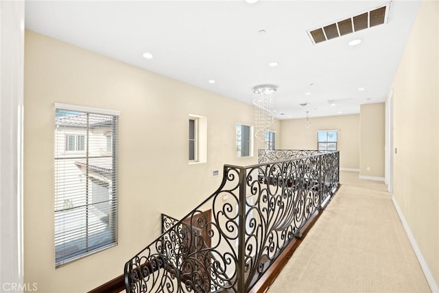 hall with plenty of natural light, light carpet, and a chandelier