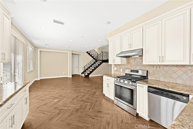 kitchen with appliances with stainless steel finishes, parquet flooring, white cabinetry, decorative backsplash, and light stone countertops