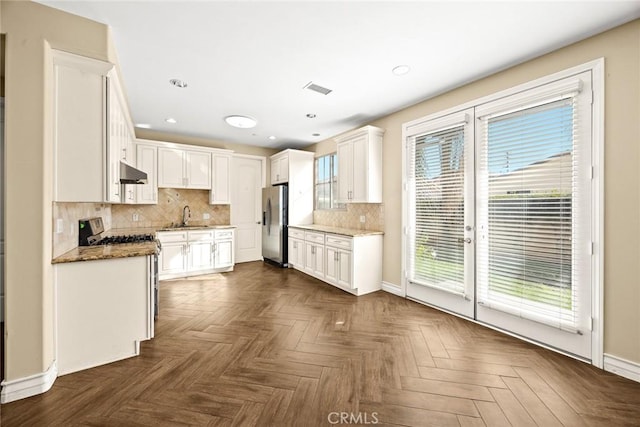 kitchen with stainless steel appliances, white cabinetry, dark parquet flooring, and dark stone countertops