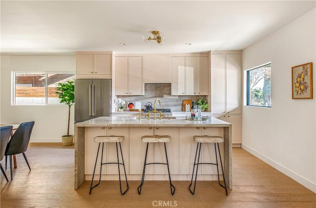 kitchen with a kitchen breakfast bar, high end fridge, a kitchen island with sink, and light stone countertops