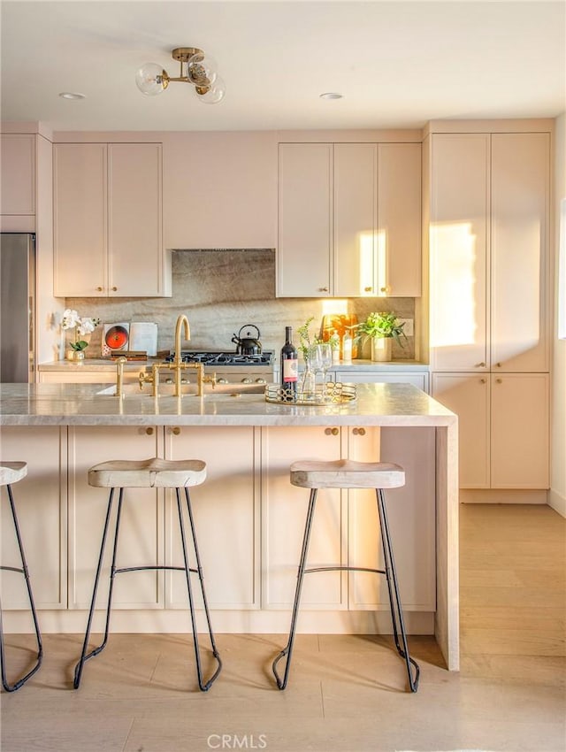 kitchen with light stone counters, stainless steel fridge, a kitchen breakfast bar, and tasteful backsplash