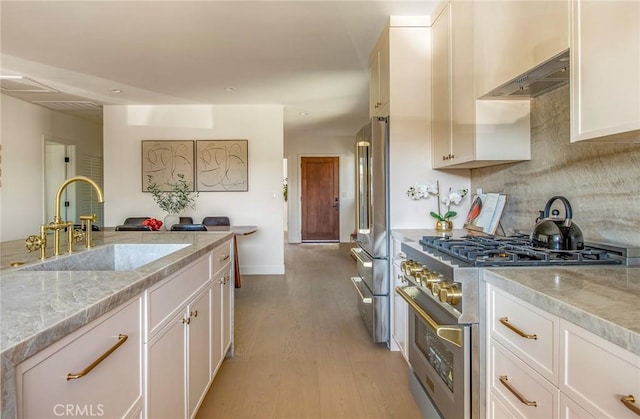 kitchen featuring sink, high end appliances, extractor fan, light stone countertops, and white cabinets