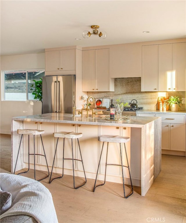 kitchen featuring tasteful backsplash, a breakfast bar area, light stone countertops, high end fridge, and light wood-type flooring