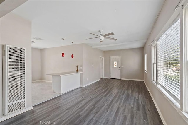 unfurnished living room with a ceiling fan, a heating unit, baseboards, and wood finished floors