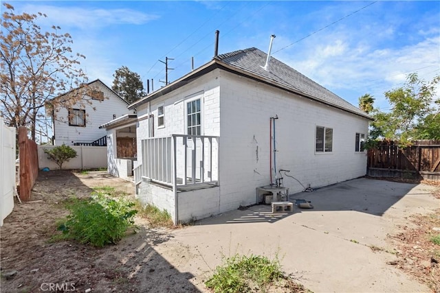 rear view of property featuring a patio, a shingled roof, concrete block siding, and a fenced backyard