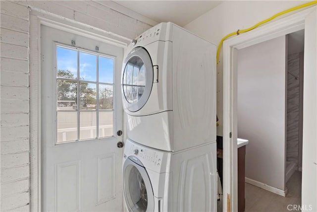 washroom featuring laundry area, stacked washer and clothes dryer, and baseboards