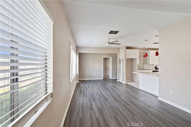 unfurnished living room featuring dark wood-style floors, ceiling fan, visible vents, and baseboards