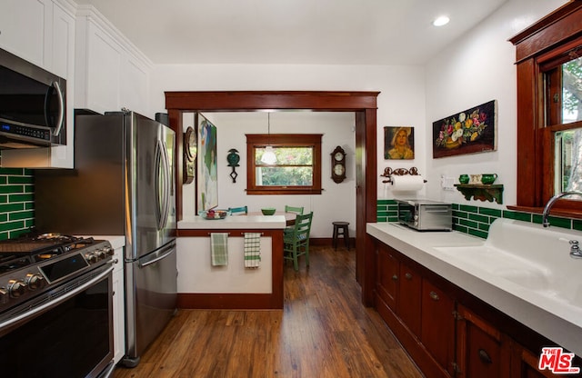 kitchen with sink, dark wood-type flooring, stainless steel appliances, decorative backsplash, and decorative light fixtures