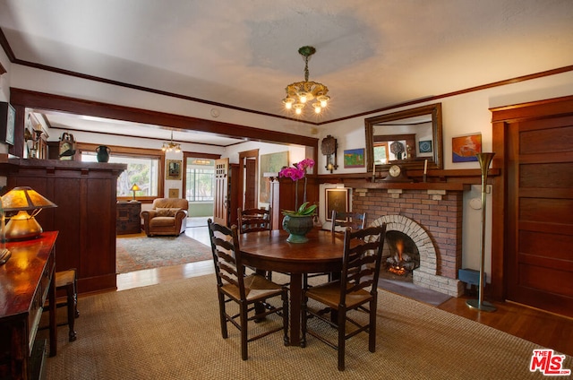 dining space featuring hardwood / wood-style flooring, crown molding, a brick fireplace, and an inviting chandelier