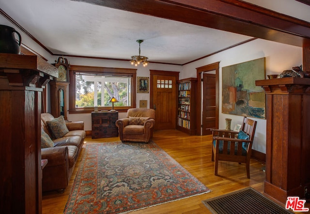 living room featuring an inviting chandelier, crown molding, decorative columns, and light hardwood / wood-style flooring