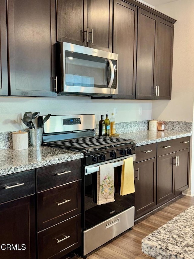 kitchen featuring appliances with stainless steel finishes, dark brown cabinets, light stone counters, and light hardwood / wood-style flooring