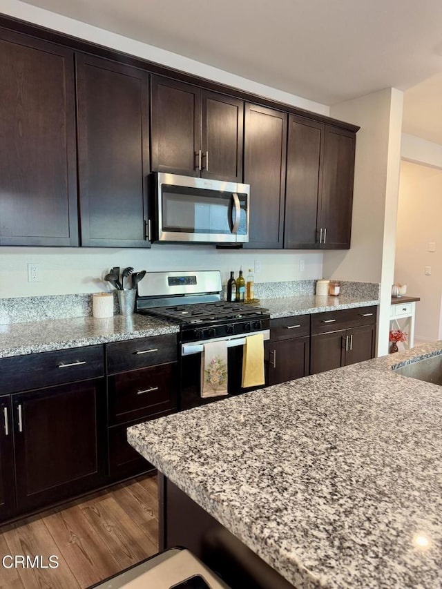 kitchen with light stone countertops, appliances with stainless steel finishes, light wood-type flooring, and dark brown cabinetry