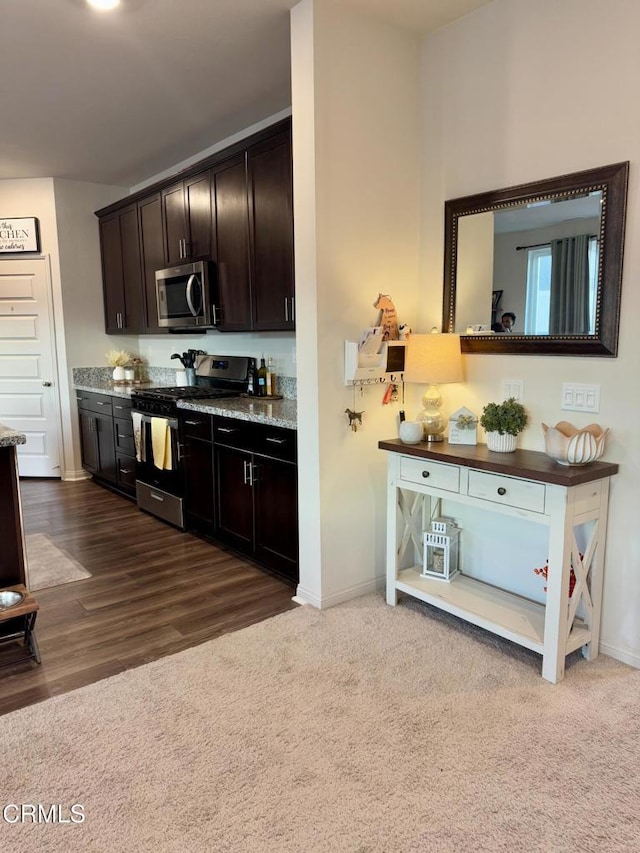 kitchen featuring stone countertops, appliances with stainless steel finishes, carpet flooring, and dark brown cabinetry