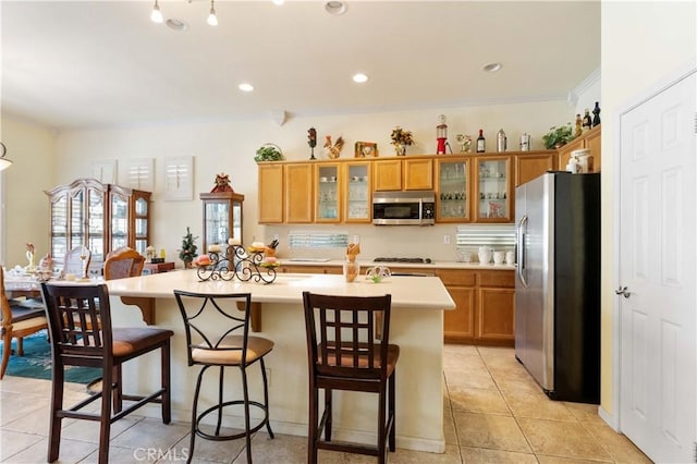 kitchen with appliances with stainless steel finishes, a breakfast bar, an island with sink, light tile patterned floors, and crown molding