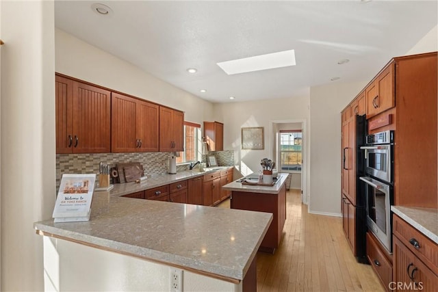 kitchen with sink, tasteful backsplash, a skylight, a center island, and kitchen peninsula