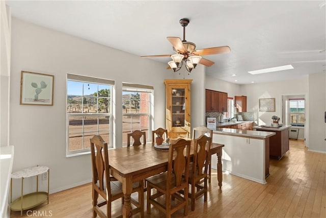 dining area with ceiling fan, plenty of natural light, light hardwood / wood-style floors, and a skylight